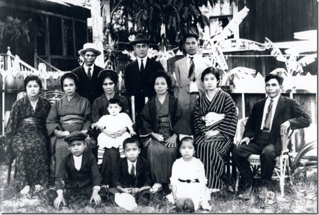 photograph of the Inafuku and Arashiro families with Mrs Wakukawa (sitting 2nd from left, Seiyei Wakukawa’s mother) was taken I believe in Honolulu in 1921 before my grandmother (4th from left), my Dad Ronald (middle sitting on ground), and my aunty Annie (young girl sitting on ground) left Hawaii to bring the remains of my grandfather Hoyei Inafuku back to Haneji Okinawa.  Grandfather Hoyei passed away from influenza in Waimea Kauai in Aug 1918. Hoichi Inafuku with the white hat is standing on the left and his younger brother Raymond Hotoku Inafuku is standing on the right.  The others in the photograph are members of the Arashiro family.  Anso Arashiro who is sitting on the right is my grandmother Kamado Arashiro Inafuku’s brother.